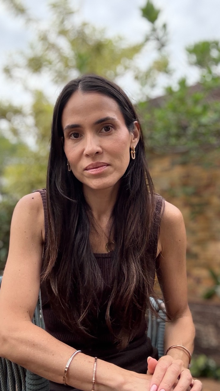 Dani Hayoshi seated outdoors, with long dark hair and a dark top, in front of trees.